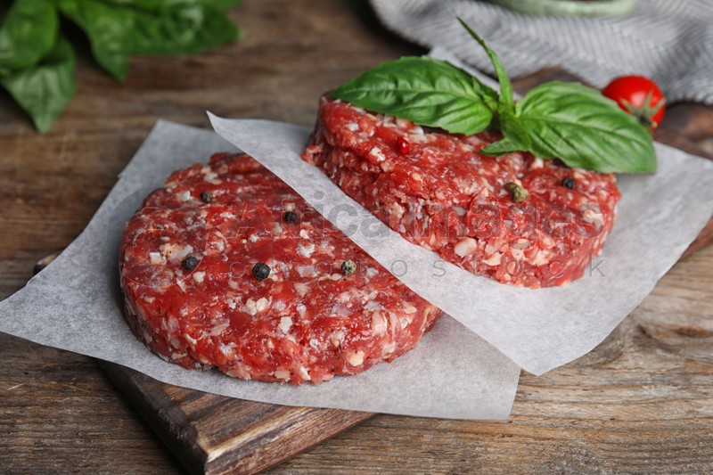 Raw meat cutlets for burger on wooden table, closeup