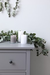 Stylish chest of drawers decorated with beautiful eucalyptus garland and candles indoors