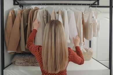 Photo of Young woman choosing outfit in dressing room, back view