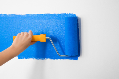 Woman painting white wall with blue dye, closeup. Interior renovation