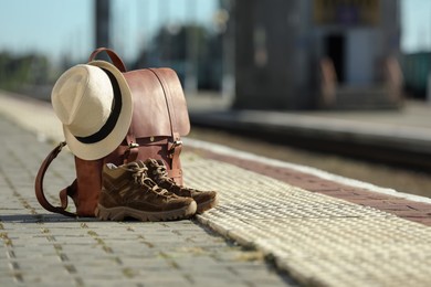 Stylish backpack, hat and shoes on railway platform outdoors. Tourism concept