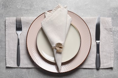 Plates with fabric napkin, decorative ring and cutlery on gray background, flat lay