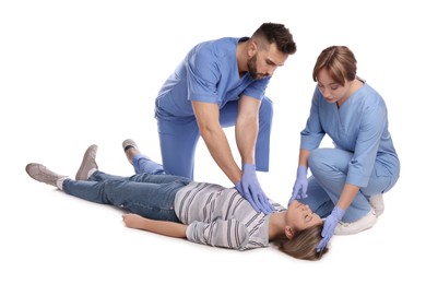 Medical workers in uniform performing first aid on unconscious woman against white background