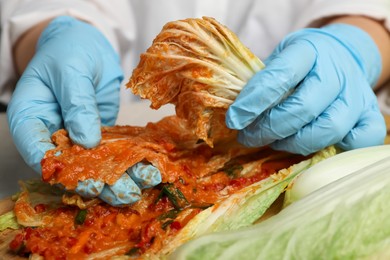 Woman preparing spicy cabbage kimchi at table, closeup