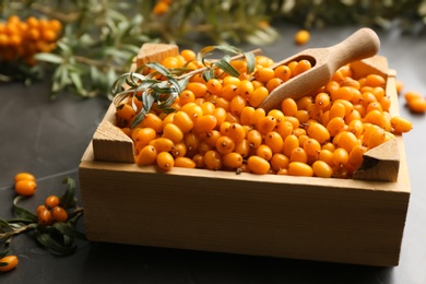Fresh ripe sea buckthorn in wooden crate on grey table, closeup
