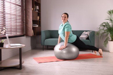 Overweight woman doing exercise with fitness ball at home