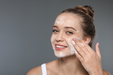 Young woman washing face with soap on grey background