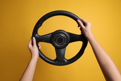 Woman holding steering wheel on yellow background, closeup