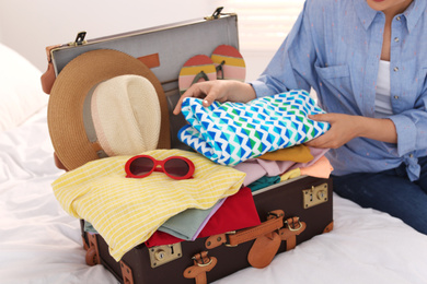 Woman packing suitcase for summer vacation in bedroom, closeup