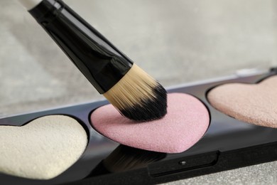 Photo of Palette of heart shaped eyeshadows with brush on grey table, closeup