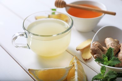 Photo of Delicious ginger tea and ingredients on white wooden table