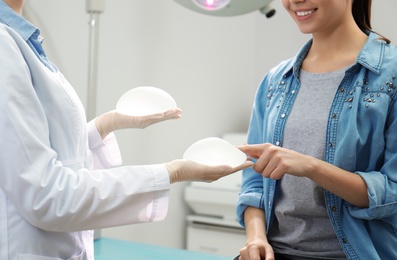 Doctor showing silicone implants for breast augmentation to patient in clinic, closeup. Cosmetic surgery