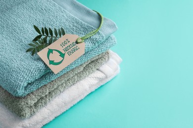 Stacked towels with recycling label and plant on turquoise background, space for text
