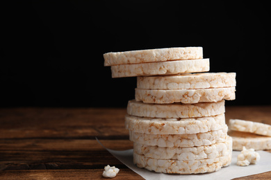 Stack of puffed rice cakes on wooden table against black background. Space for text