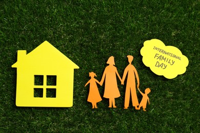 Card with text International Family Day, paper cutout and wooden house figure on green grass, flat lay