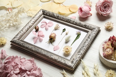 Composition with beautiful dry flowers and vintage frame on white wooden background
