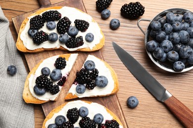 Tasty sandwiches with cream cheese, blueberries and blackberries on wooden table, flat lay