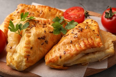 Photo of Fresh delicious puff pastry with cheese, tomatoes and parsley on wooden board, closeup