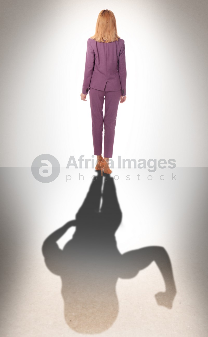Businesswoman and shadow of strong muscular lady behind her on light background. Concept of inner strength