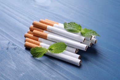 Menthol cigarettes and mint leaves on blue wooden table
