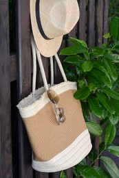 Stylish bag with hat and sunglasses hanging on wooden fence outdoors. Beach accessories