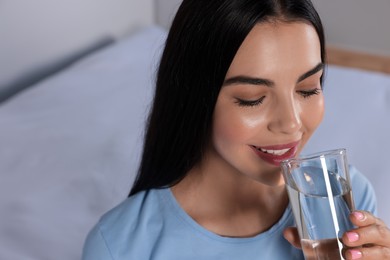 Young woman drinking water indoors, closeup. Refreshing drink
