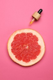 Pipette with citrus essential oil and fresh grapefruit slice on pink background, flat lay