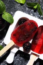 Mold with tasty blackberry ice pops on dark textured table, flat lay. Fruit popsicle