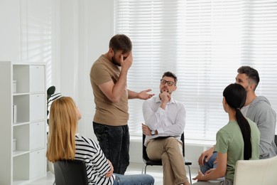 Psychotherapist working with group of drug addicted people at therapy session indoors