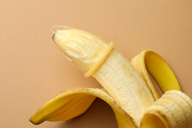 Banana with condom on pale orange background, closeup. Safe sex concept