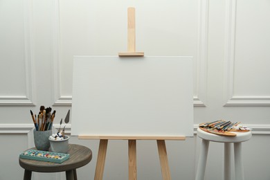 Easel with blank canvas, brushes, paints and palette in studio