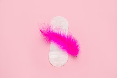 Sanitary pad with feather on pink background, top view. Menstrual cycle