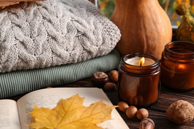 Photo of Burning scented candles, warm sweaters, book and pumpkins on wooden table. Autumn coziness