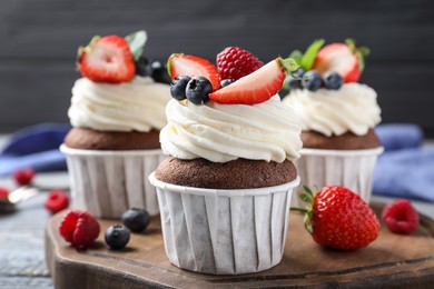 Sweet cupcakes with fresh berries on wooden board, closeup