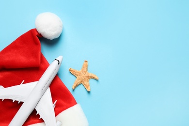 Santa hat with toy airplane, starfish and space for text on light blue background, flat lay. Christmas vacation