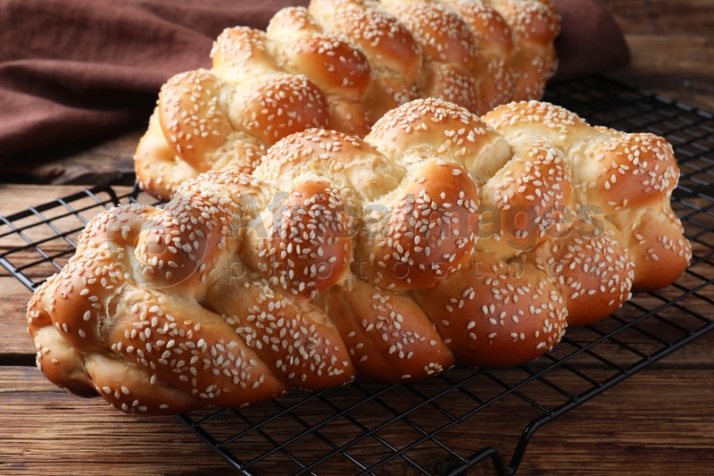 Photo of Homemade braided breads with sesame seeds on wooden table, closeup. Challah for Shabbat