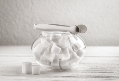 Refined sugar cubes in glass bowl and tongs on white wooden table
