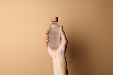 Woman holding bottle of cosmetic product on beige background, closeup