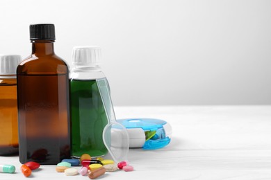Photo of Bottles of syrup, dosing spoon and pills on white table against light grey background, space for text. Cold medicine