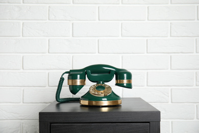 Green vintage corded phone on small black table near white brick wall