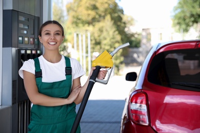 Young worker with fuel pump nozzle near car at modern gas station
