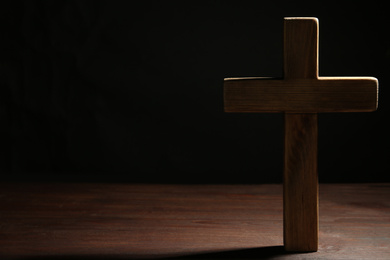 Christian cross on wooden table against black background, space for text. Religion concept