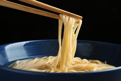Photo of Eating noodle dish with chopsticks against black background, closeup