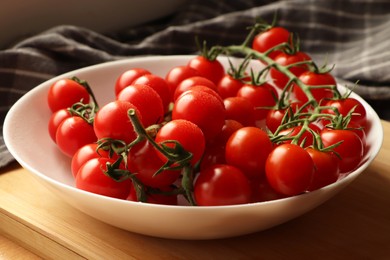 Plate of ripe whole cherry tomatoes with water drops on wooden table, closeup