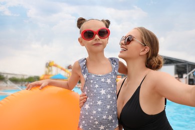 Mother and daughter with inflatable ring near pool in water park. Family vacation