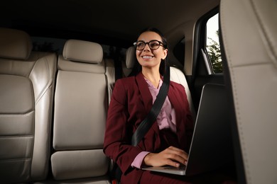 Young woman working on laptop in modern taxi, space for text