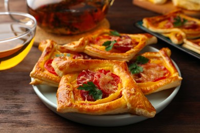 Photo of Fresh delicious puff pastry with cheese, tomatoes and parsley on wooden table, closeup