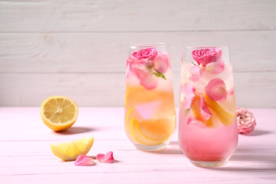 Delicious refreshing drink with lemon and roses on pink wooden table