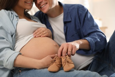 Young pregnant woman and her husband with baby's shoes, closeup