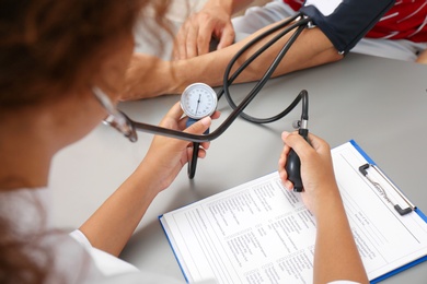 Doctor checking patient's blood pressure at table in office, closeup